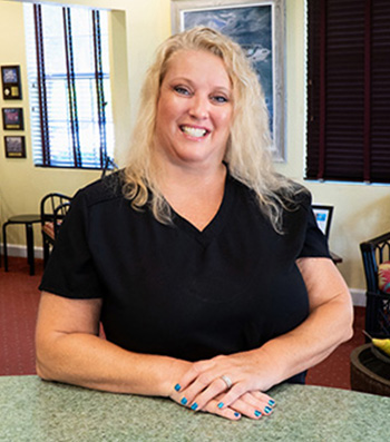 A smiling woman in a black shirt and white pants stands behind a counter.