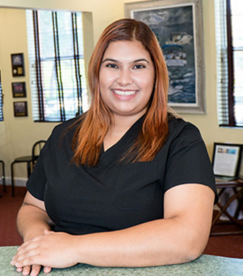 A woman wearing a black shirt and smiling at the camera, standing in front of a counter with a framed picture on the wall.