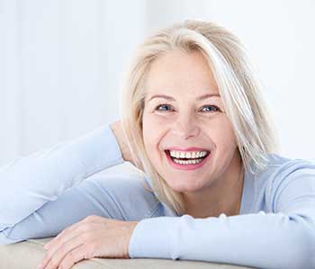 A smiling woman with blonde hair leaning on a couch.