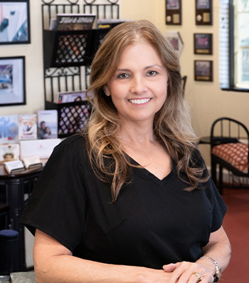 A woman with blonde hair is standing in a room, smiling at the camera.