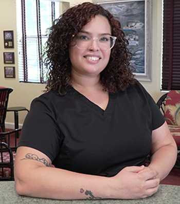 A woman in a black shirt, glasses, and tattooed arm is standing behind a counter.