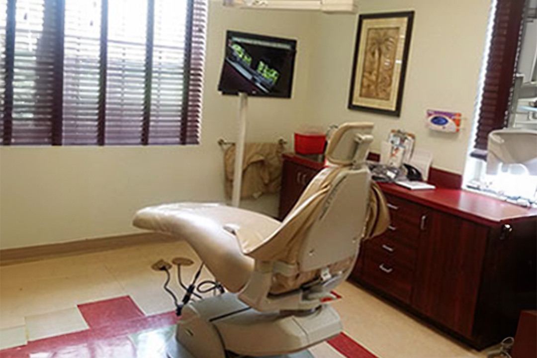 The image shows a dental office with a modern dental chair, a computer monitor displaying an image of a mouth, and various dental equipment.