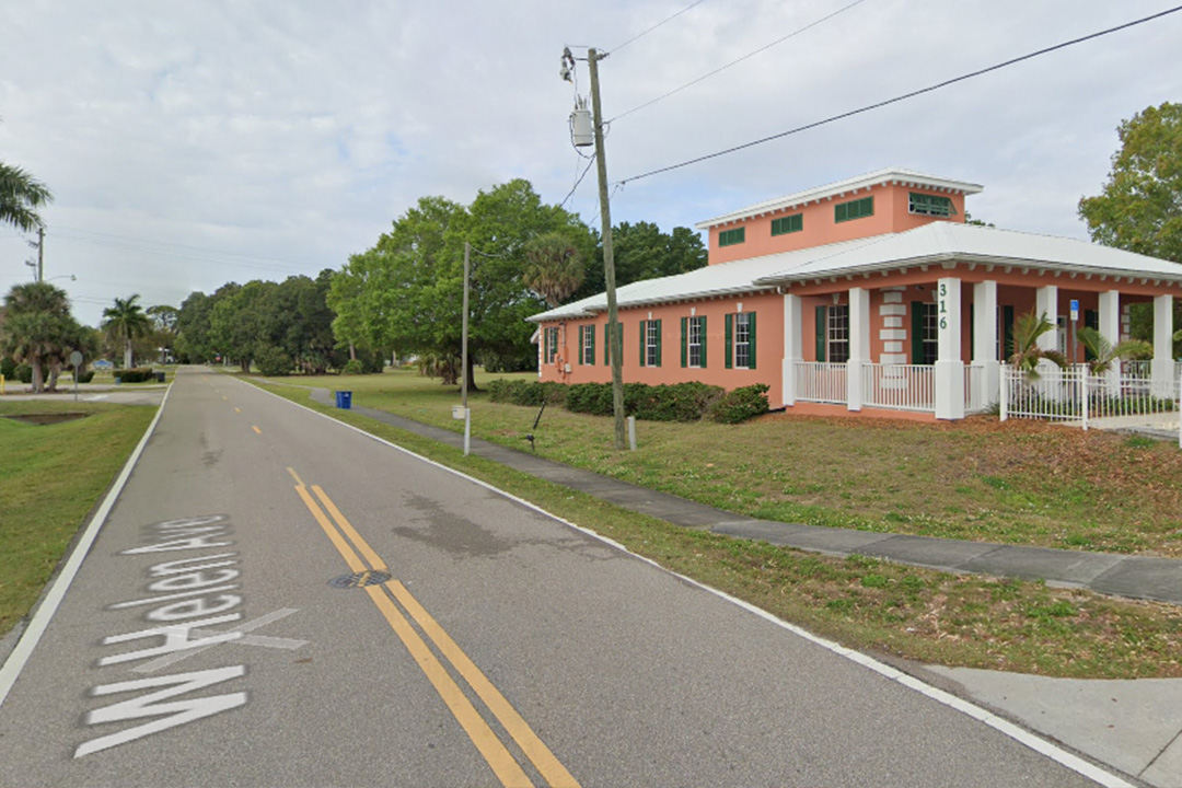 The image shows a two-story building with a prominent front porch, situated on a street corner.