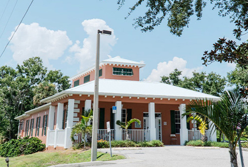 The image shows a single-story building with a white roof and a prominent tower, set against a clear blue sky.