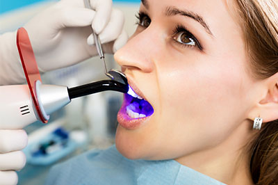 A woman receiving a dental procedure with an instrument in her mouth, surrounded by medical equipment and personnel.