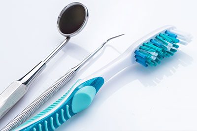 The image shows a collection of dental tools, including a toothbrush with blue bristles and a pair of scissors, laid out on a white surface.