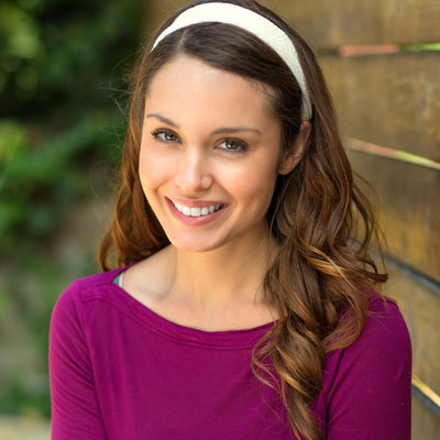The image features a woman with long hair smiling at the camera, wearing a purple top and a white headband.