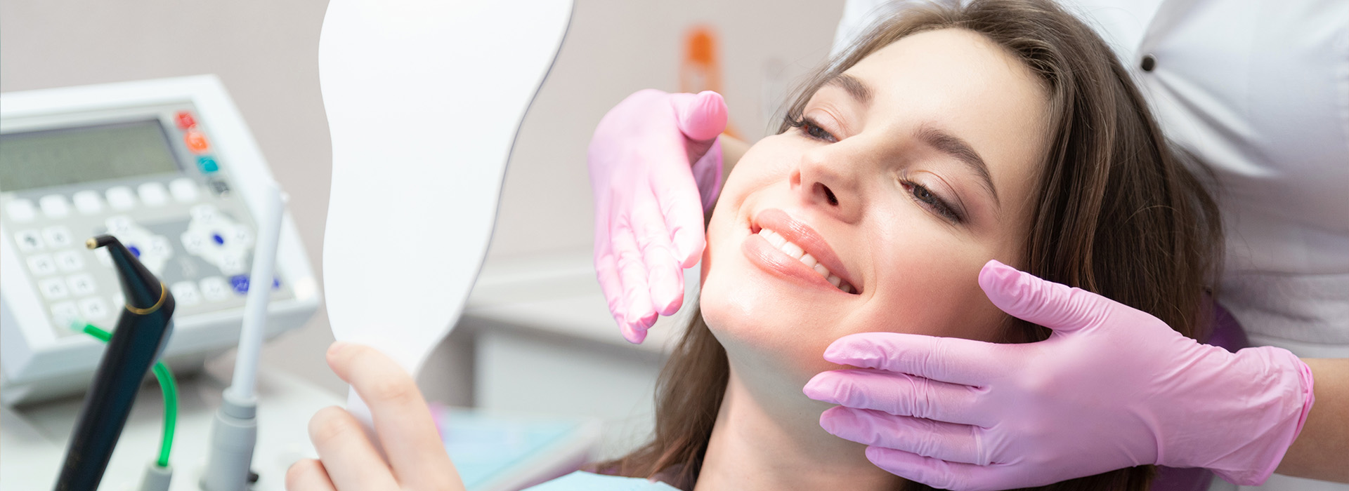 A woman is seated in a dental chair, receiving dental care with her mouth open.