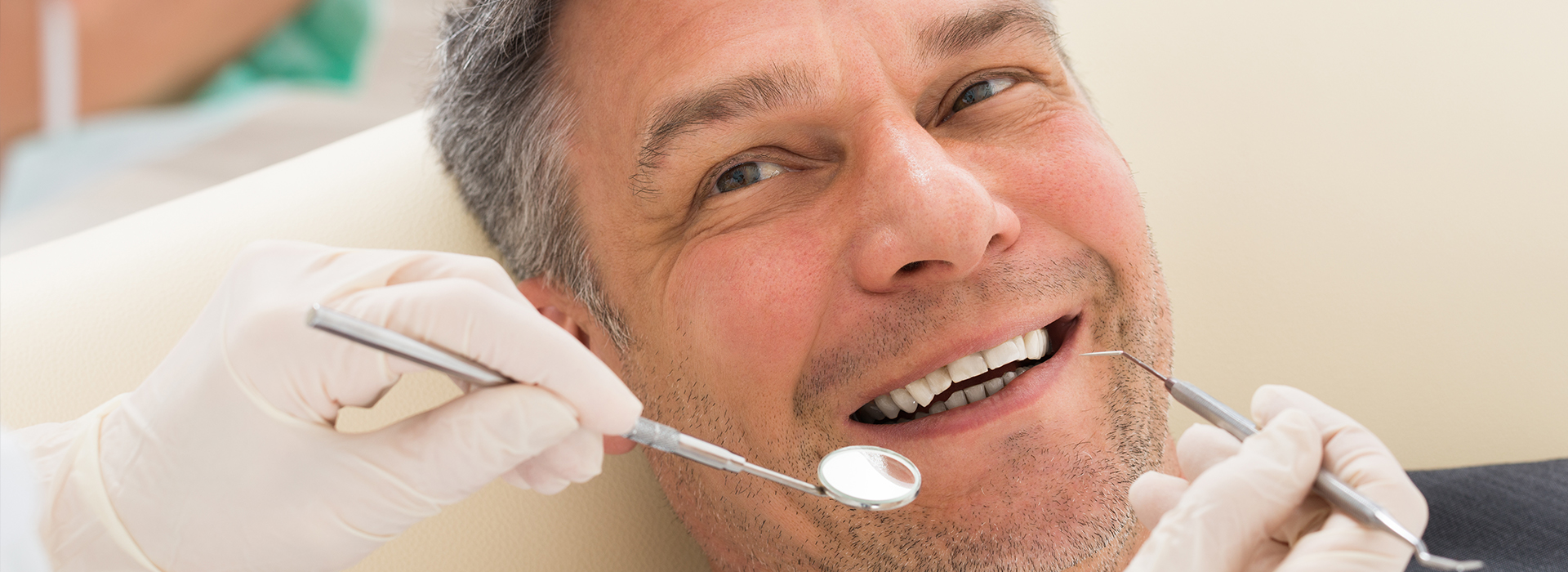 A man undergoing dental treatment, smiling at the camera while a dental professional works on his teeth.