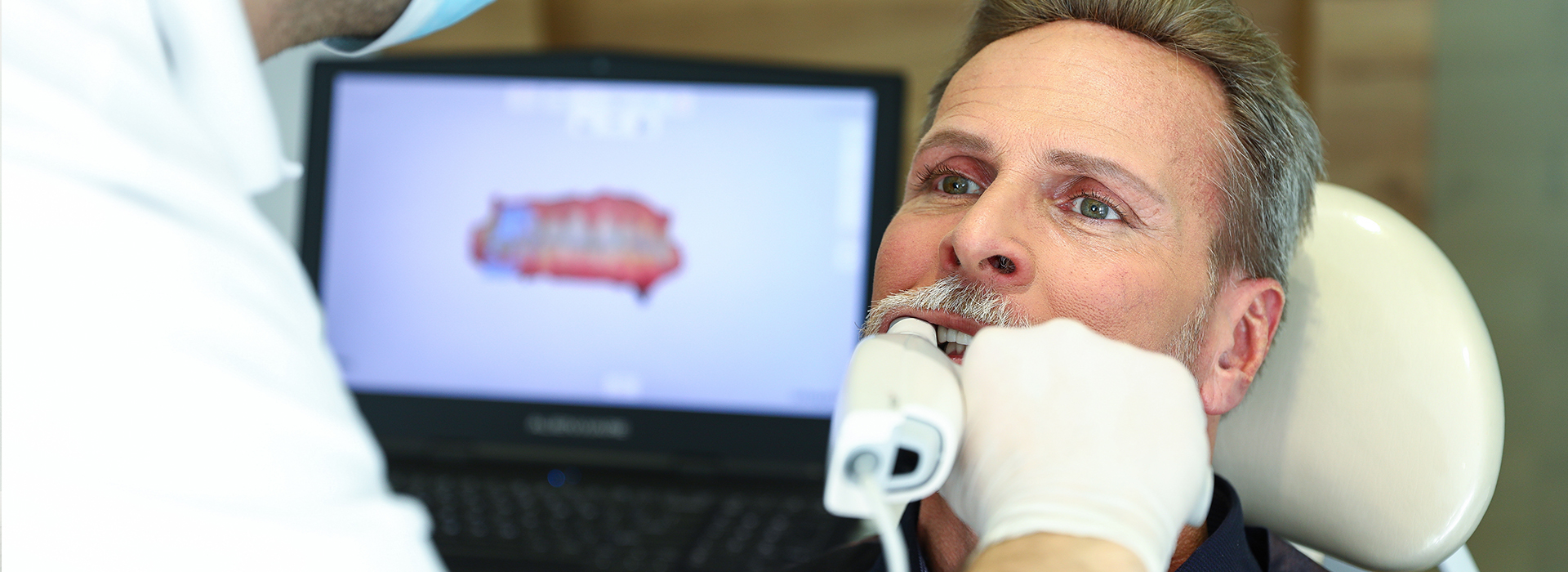 A man receiving dental care, with a dental professional using a computer screen to guide the procedure.