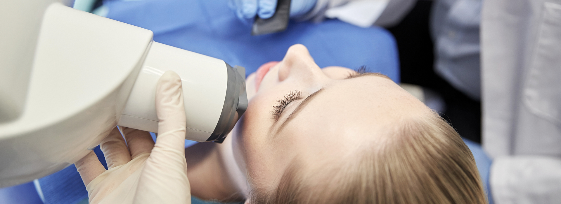 A person receiving a dental examination, with a dentist using a magnified viewer to inspect their teeth.
