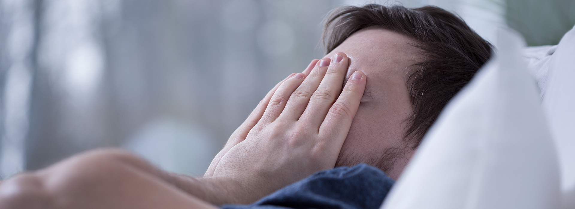 A person lying in bed with hands covering their face, appearing to be asleep or resting.