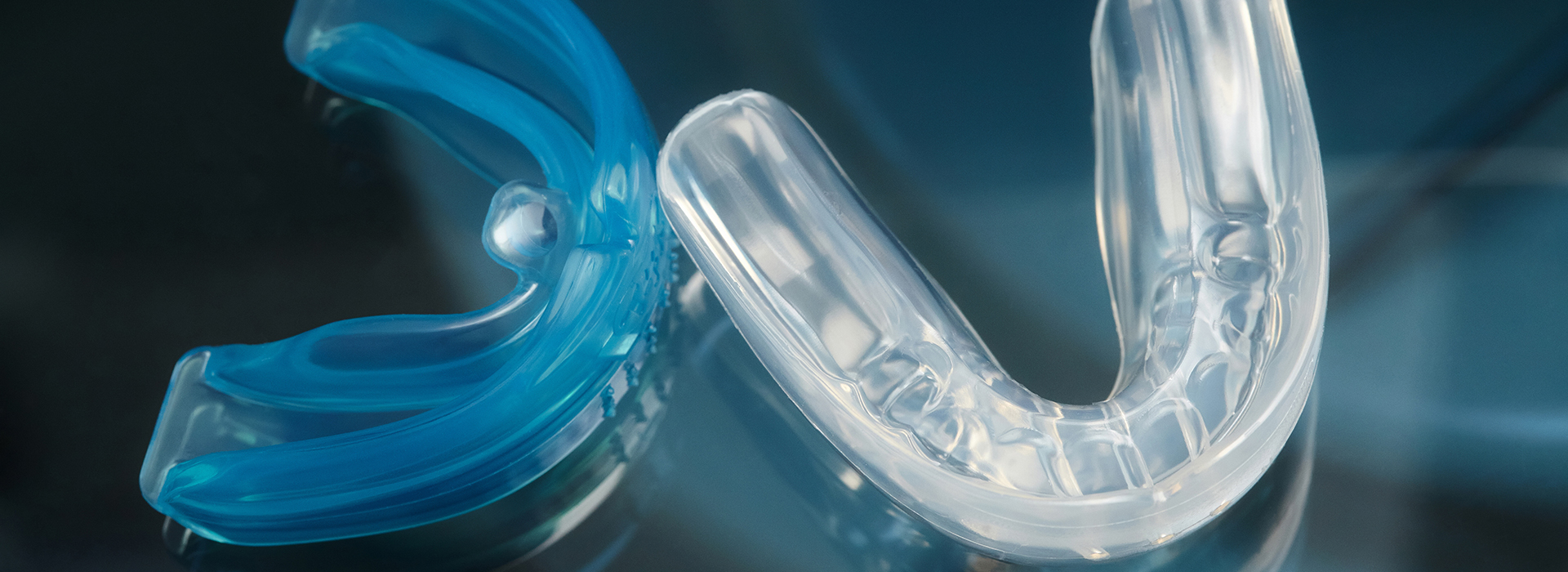 A close-up photograph of a blue and clear plastic object with a curved shape, resembling a toothbrush head or a part of a cleaning appliance.