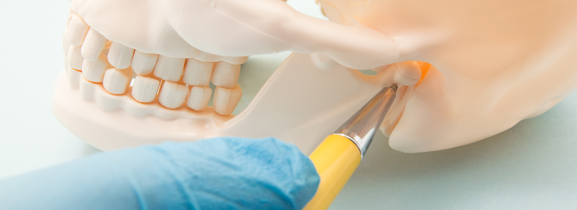 The image shows a close-up of a dental procedure in progress, with a hand holding a yellow instrument near a tooth model.