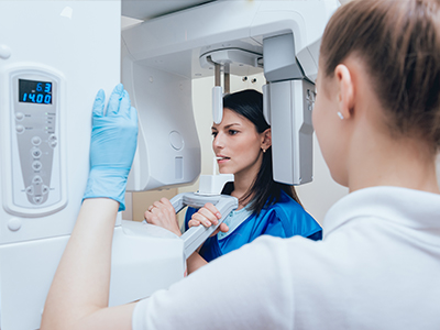 A woman in a blue coat and white gloves is operating a large, modern 3D scanner machine, while another person looks on.