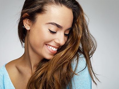 The image shows a close-up of a woman with long hair, smiling and looking away from the camera. She is wearing what appears to be a light blue top.
