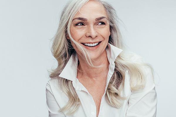 The image is a portrait of a woman with light hair, wearing a white shirt and smiling at the camera.