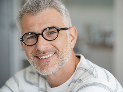 A smiling man with gray hair, wearing glasses and a white shirt, poses for the camera.