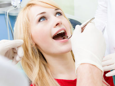 A woman is sitting in a dental chair, receiving dental care, with a smile on her face.
