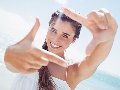 A woman is taking a selfie with her hand held up to the camera, smiling and appearing joyful.