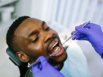 The image shows a person in a dental chair receiving dental treatment, with a dentist working on their teeth and a nurse assisting.